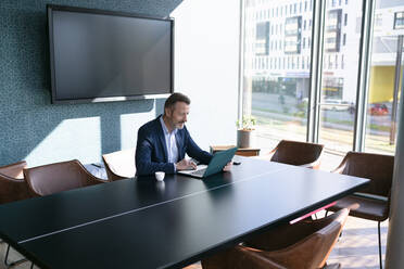 Male entrepreneur using laptop at conference table in office - FKF04350