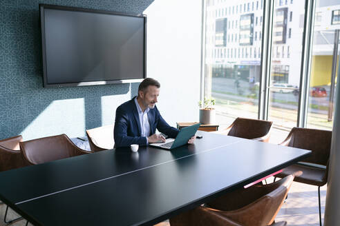 Männlicher Unternehmer mit Laptop am Konferenztisch im Büro - FKF04350