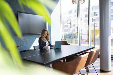 Smiling businesswoman having coffee while working on laptop at office - FKF04358