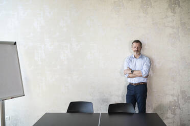 Businessman with arms crossed standing in front of wall at office - FKF04361