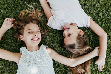 Happy girls lying on grass in summer - EBBF03746