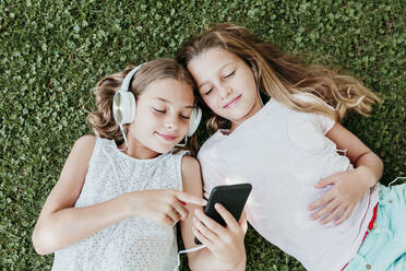 Smiling friends listening music while lying on grass in summer - EBBF03748