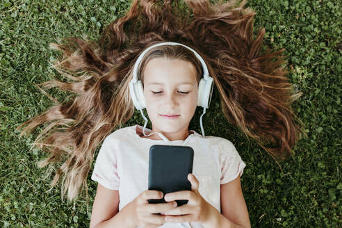 Mädchen mit Kopfhörern hört Musik, während sie im Gras liegt - EBBF03752