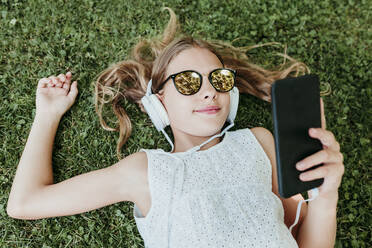 Girl wearing sunglasses lying on grass in summer - EBBF03754