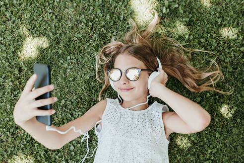 Lächelndes Mädchen, das ein Handy benutzt, während es im Gras liegt - EBBF03757