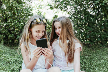 Cheerful girl with friend using mobile phone in garden - EBBF03763