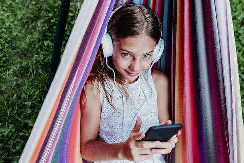 Lächelndes Mädchen hört Musik beim Entspannen in der Hängematte - EBBF03770