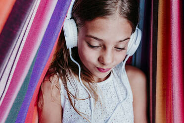 Smiling girl listening music while relaxing in multi colored hammock - EBBF03771