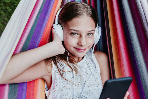 Braunäugiges Mädchen hört Musik und entspannt sich in einer bunten Hängematte - EBBF03772