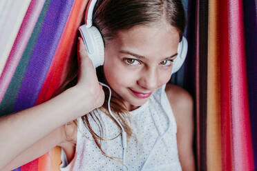 Smiling girl enjoying listening music in hammock - EBBF03773