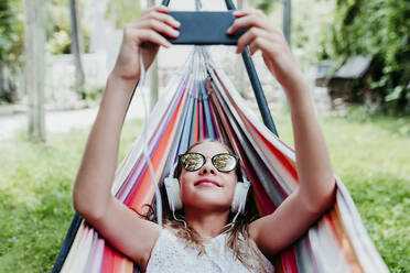 Girl wearing sunglasses using mobile phone in hammock at garden - EBBF03774