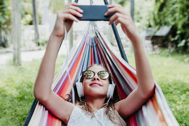 Mädchen mit Sonnenbrille und Mobiltelefon in der Hängematte im Garten - EBBF03774