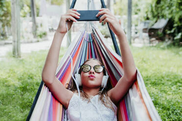 Girl wearing sunglasses puckering while using mobile phone in garden - EBBF03775