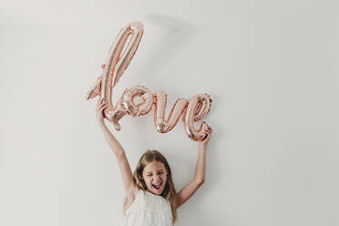 Cheerful girl with love balloon in front of wall - EBBF03783