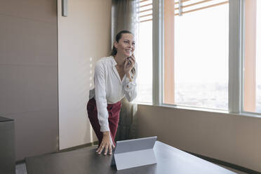 Smiling female entrepreneur talking on mobile phone at desk in office - JRVF00796