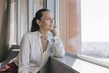 Schöne Unternehmerin schaut durch das Fenster, während sie im Büro sitzt - JRVF00799