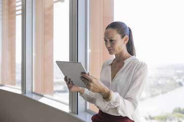 Ältere Unternehmerin benutzt digitales Tablet am Fenster im Büro - JRVF00802