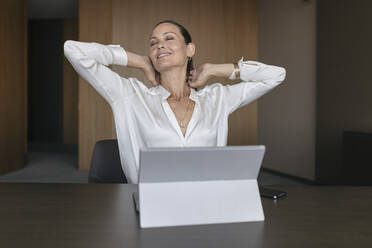 Happy businesswoman sitting with eyes closed at desk in office - JRVF00837