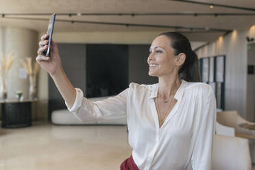 Lächelnde Geschäftsfrau nimmt Selfie durch Smartphone in der Lobby - JRVF00852