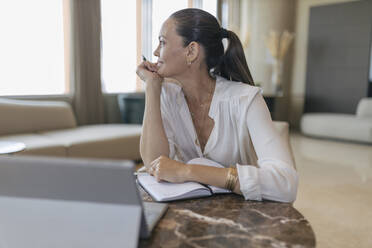 Thoughtful female professional sitting with diary at table in lobby - JRVF00863