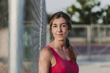 Female athlete by fence in stadium - EBBF03795