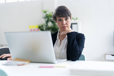 Businesswoman sitting with hand on chin at desk in office - GIOF12678