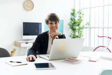 Businesswoman sitting with laptop at desk in office - GIOF12680