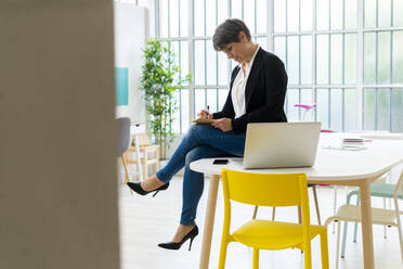 Female professional writing while siting on desk in office - GIOF12682