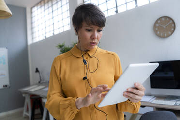 Businesswoman wearing in-ear headphones using digital tablet while working in office - GIOF12696