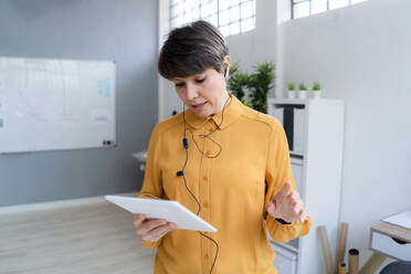 Female entrepreneur wearing in-ear headphones on video call through digital tablet in office - GIOF12697