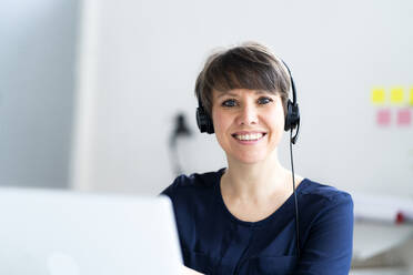 Lächelnde Frau mit kurzen Haaren und Headset im Büro - GIOF12703