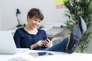 Lächelnde weibliche Fachkraft, die im Büro mit ihrem Handy im Internet surft - GIOF12706