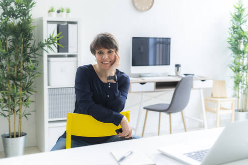 Lächelnde Geschäftsfrau sitzt auf einem Stuhl im Büro - GIOF12708