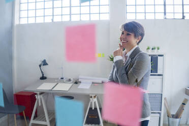 Happy female entrepreneur looking away while standing with hand on chin office - GIOF12711