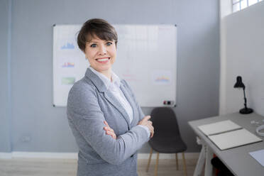 Smiling female professional standing with arms crossed in office - GIOF12712