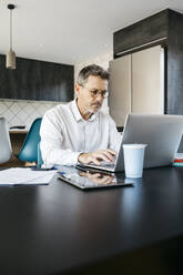 Geschäftsmann arbeitet am Laptop in der heimischen Küche im Home Office - JRFF05131