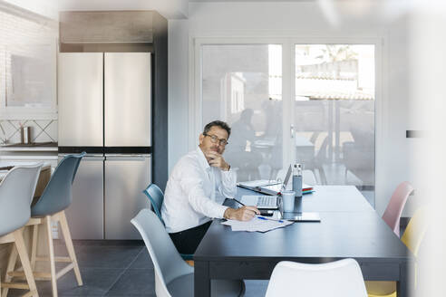 Geschäftsmann, der wegschaut, während er am Tisch im Heimbüro sitzt - JRFF05144