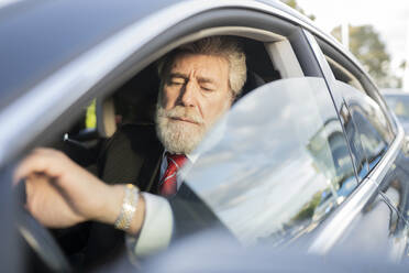 Mature businessman looking at wristwatch while driving car in city - JCCMF02609