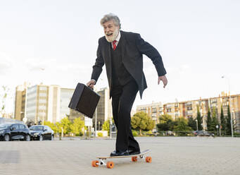 Glücklicher Geschäftsmann, der mit dem Skateboard in der Stadt unterwegs ist - JCCMF02618