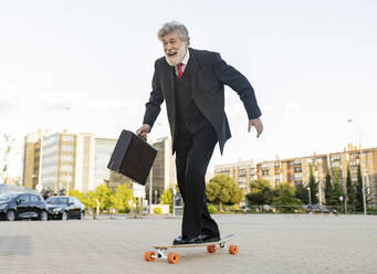 Happy businessman commuting on skateboard in city - JCCMF02618