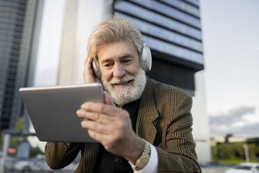 Smiling male professional listening through headphones while using digital tablet in city - JCCMF02629