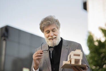 Smiling mature bearded architect looking at model house - JCCMF02635