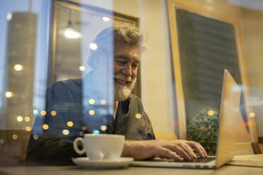 Lächelnde männliche Fachkraft, die einen Laptop benutzt, während sie in einem Café arbeitet - JCCMF02653