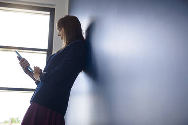 Young female professional using digital tablet while leaning on wall in office - BMOF00823