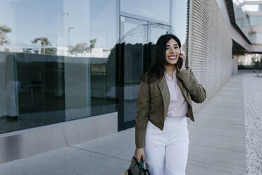 Female professional with bag talking on mobile phone - TCEF01876