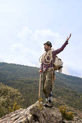 Male mountaineer standing with hand raised on mountain - VEGF04566