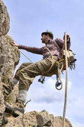 Männlicher Bergsteiger mit Sicherheitsgurt beim Bergsteigen an einem sonnigen Tag - VEGF04575