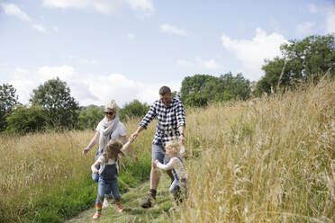 Glückliche Familie beim Laufen in einem sonnigen ländlichen Gebiet - CAIF30348