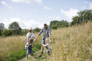 Happy family running in sunny rural field - CAIF30348