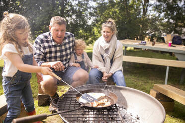 Glückliche Familie beim Grillen auf dem sonnigen Campingplatz - CAIF30349